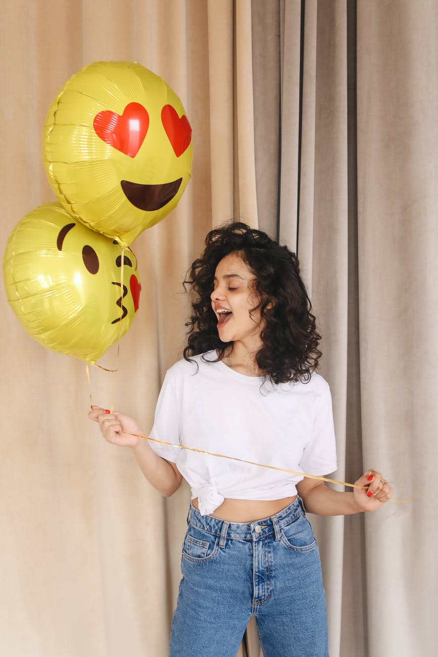 woman in white shirt and blue denim shorts holding yellow balloons